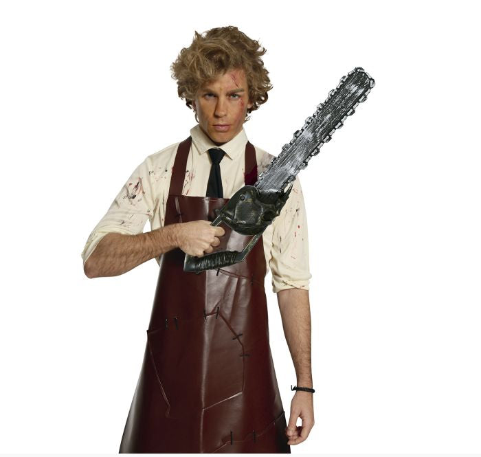 A man modeling a Leatherface-style costume against a white background, wearing a dark brown apron over a blood-splattered cream shirt and black tie, while holding a chainsaw prop.
