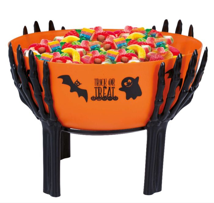 An orange Halloween bowl with black skeletal hands holding it, filled with colorful gummy candies. The bowl has black bat and ghost graphics with the words 'TRICK OR TREAT' on the front.