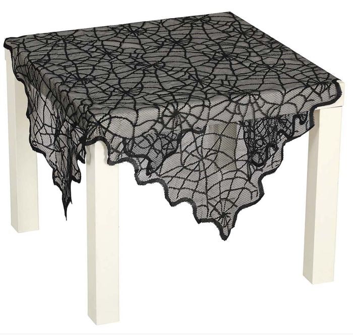 Black lace tablecloth with a spiderweb pattern draped over a white table on a white background.