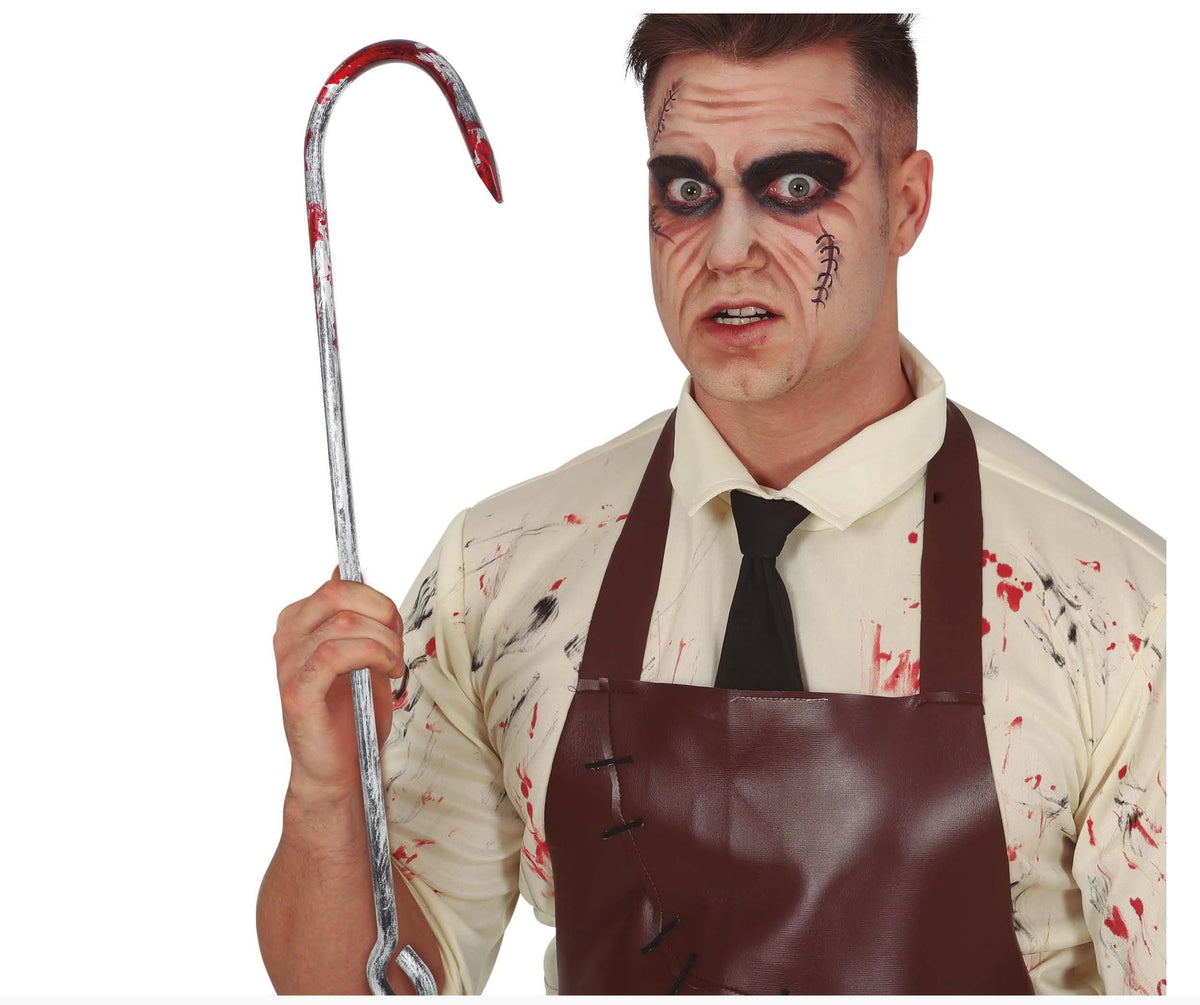A man wearing a zombie Halloween costume with blood-splattered makeup, a cream shirt, black tie, and brown apron, holding a metal crowbar prop with red fake blood splatter, against a white background.
