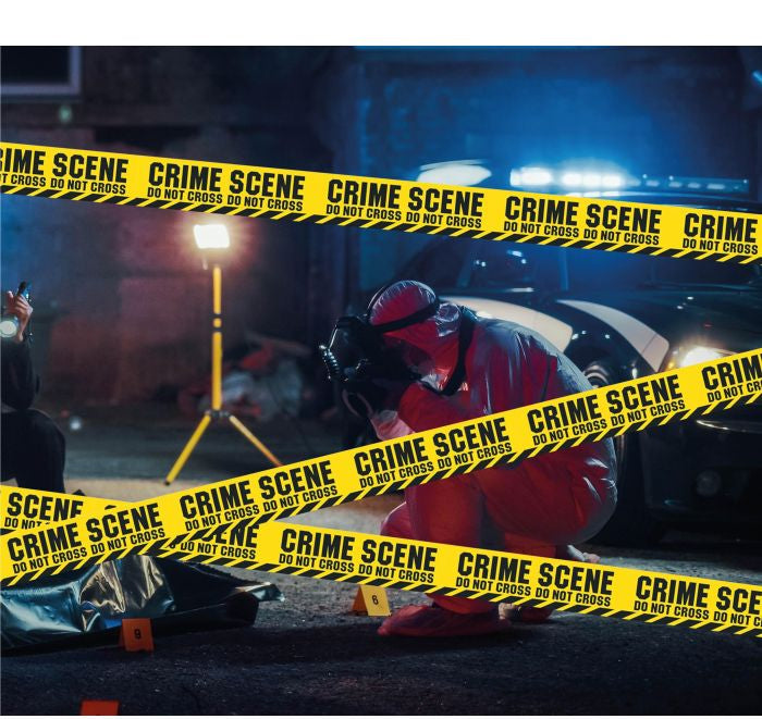 A person in a red protective suit kneels at a crime scene with police tape reading 'CRIME SCENE DO NOT CROSS' across the frame. A flashlight, evidence bag, and vehicle are visible in a dark outdoor nighttime setting.