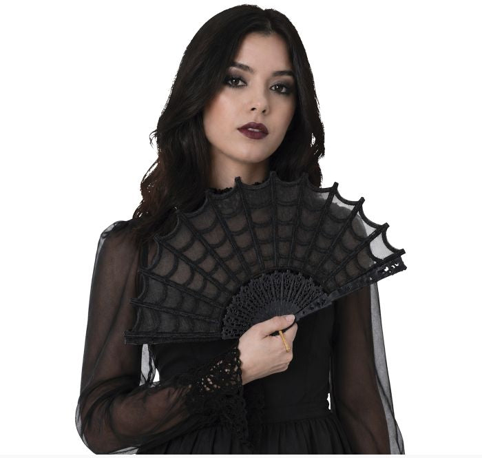 A woman with dark hair wearing a black sheer long-sleeve dress and holding a black lace spiderweb fan against a white background.