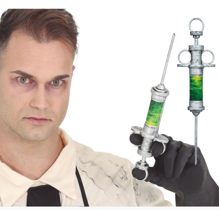A man in a white shirt and black tie holds a silver syringe prop filled with green liquid, with a second matching syringe prop floating beside him on a white background. A copyright notice for Fiestas Guirca s.