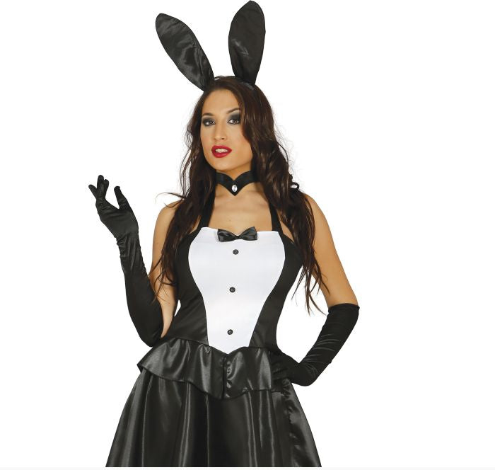 A woman modeling a black and white bunny costume with black satin bunny ears, long black gloves, a black choker, and a black-and-white ruffled dress against a plain white background.