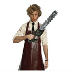A man modeling a Leatherface-style costume against a white background, wearing a dark brown apron over a blood-splattered cream shirt and black tie, while holding a chainsaw prop. 
