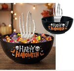 Black Halloween-themed candy bowl with 'Happy Halloween' text, skull and bat graphics, and two white skeleton hand props rising from the candy. A smaller inset shows the bowl alone with one hand inserted.