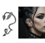 A gothic dragon ear cuff in silver-tone metal, shown both as a standalone product on the left and worn on a model's ear on the right. The model has dark hair, black eye makeup, and a black lace collar.