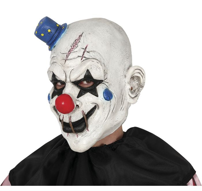 A scary clown mask with a white face, black eye makeup, a red nose, blue cheek dots, a small blue top hat, and a stitched mouth, shown on a model wearing a black cape against a white background.