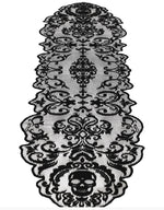 Black lace table runner with an ornate baroque damask pattern and a skull motif at the bottom, shown on a white background.