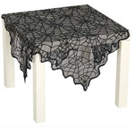 Black lace tablecloth with a spiderweb pattern draped over a white table on a white background.