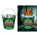 A green and black 'Deadly Potions' metal bucket cooler with a silver handle, shown on a white background and also pictured filled with beer bottles in ice against a spooky forest backdrop.