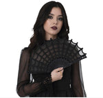 A woman with dark hair wearing a black sheer long-sleeve dress and holding a black lace spiderweb fan against a white background.