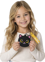 A young girl with long blonde hair holds a small black cat-shaped coin purse with a yellow keychain tag. The purse has pink ears, yellow eyes, and a white nose.