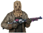 A person wearing a distressed brown hooded mask and dirty work clothes holds a shotgun with a colorful skull-and-floral graphic wrap. The background is plain white, with a copyright watermark for Fiestas Guirca at the bottom.