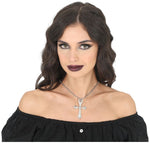 A woman with dark wavy hair and dark lipstick wears a silver cross pendant necklace with clear crystals, paired with a black off-the-shoulder top against a white background.