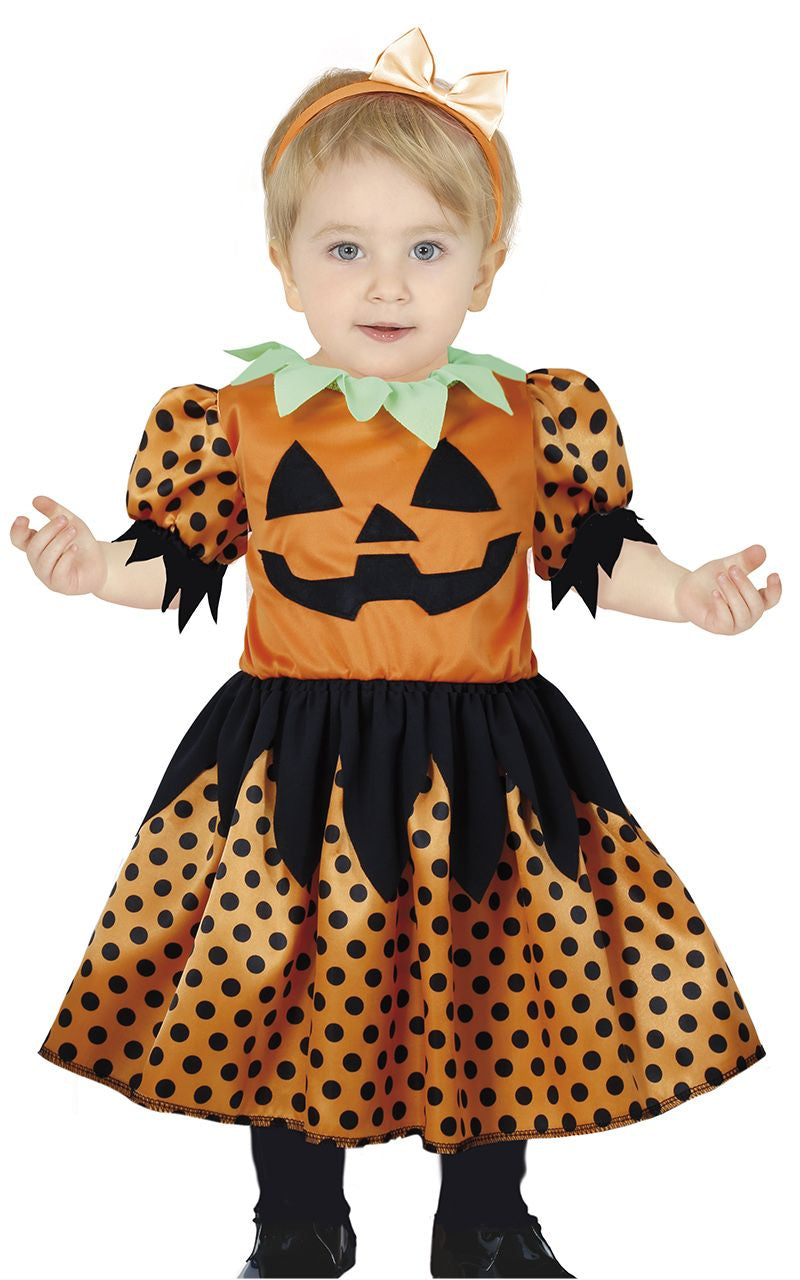 Child wearing a Halloween-themed dress with pumpkin face design on a white background