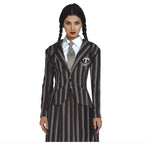A woman modeling a Wednesday Addams-style costume consisting of a dark gray and black pinstriped blazer with a white shirt, striped tie, and a matching skirt. A circular skull-and-crossbones patch is pinned to the blazer.