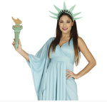 A woman modeling a light blue Statue costume with a matching green crown and holding a toy torch, against a plain white background.